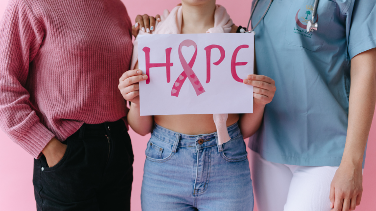 tres mujeres sosteniendo un cartel que dice "hope" con una cinta rosa simbolizando el cáncer de mama